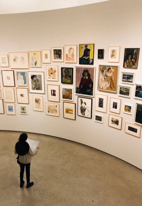 Unrecognizable woman near wall with collection of pictures in gallery